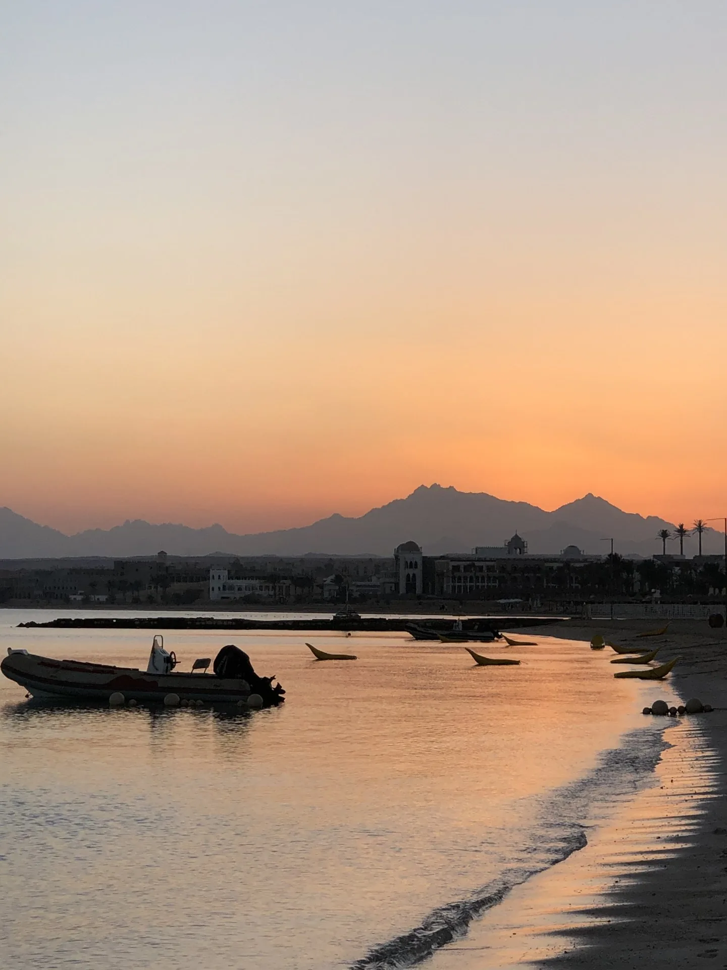 Small boats on calm coastal water beneath an orange sunset