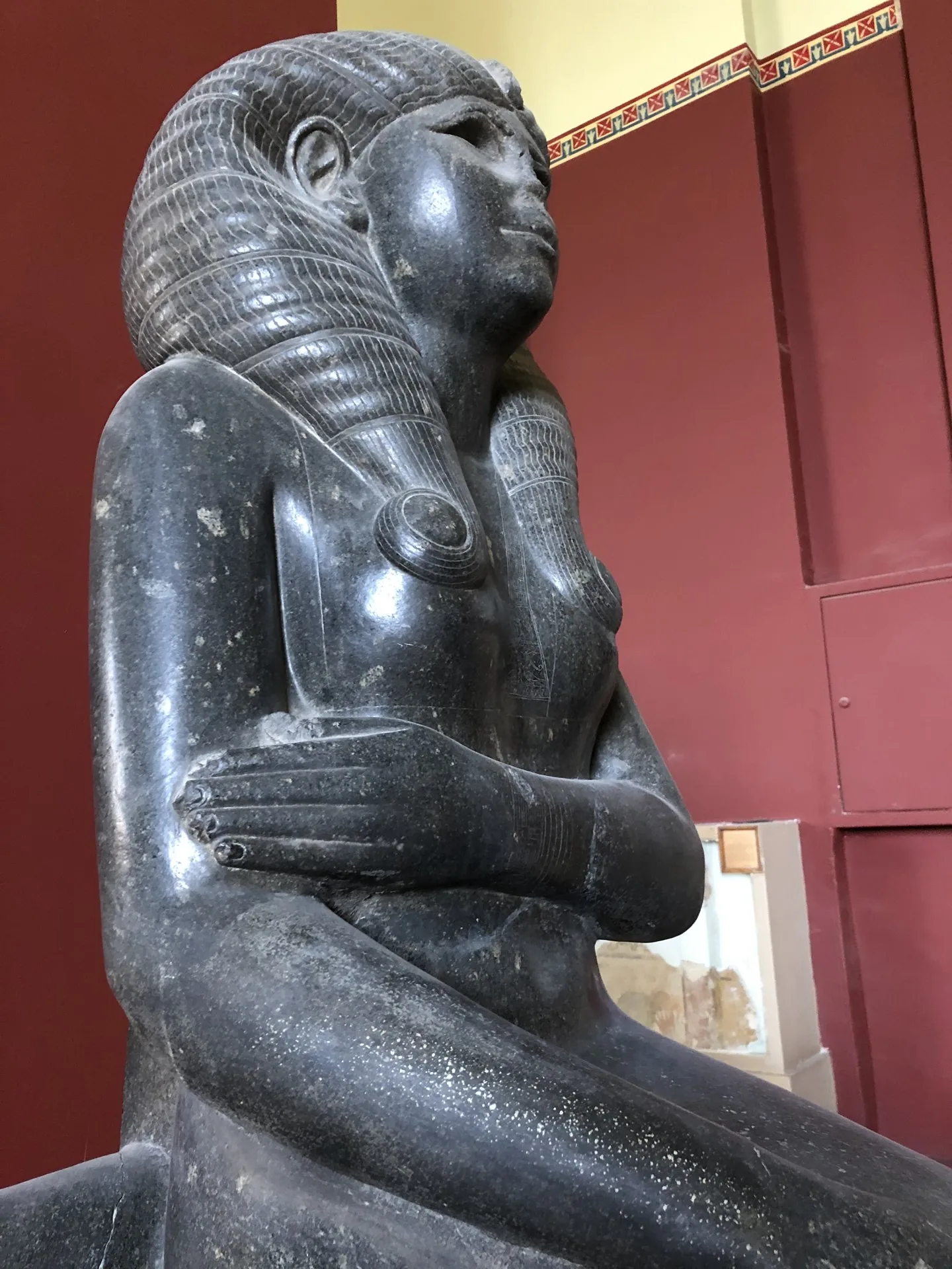 A dark stone statue with a carved headdress inside a museum